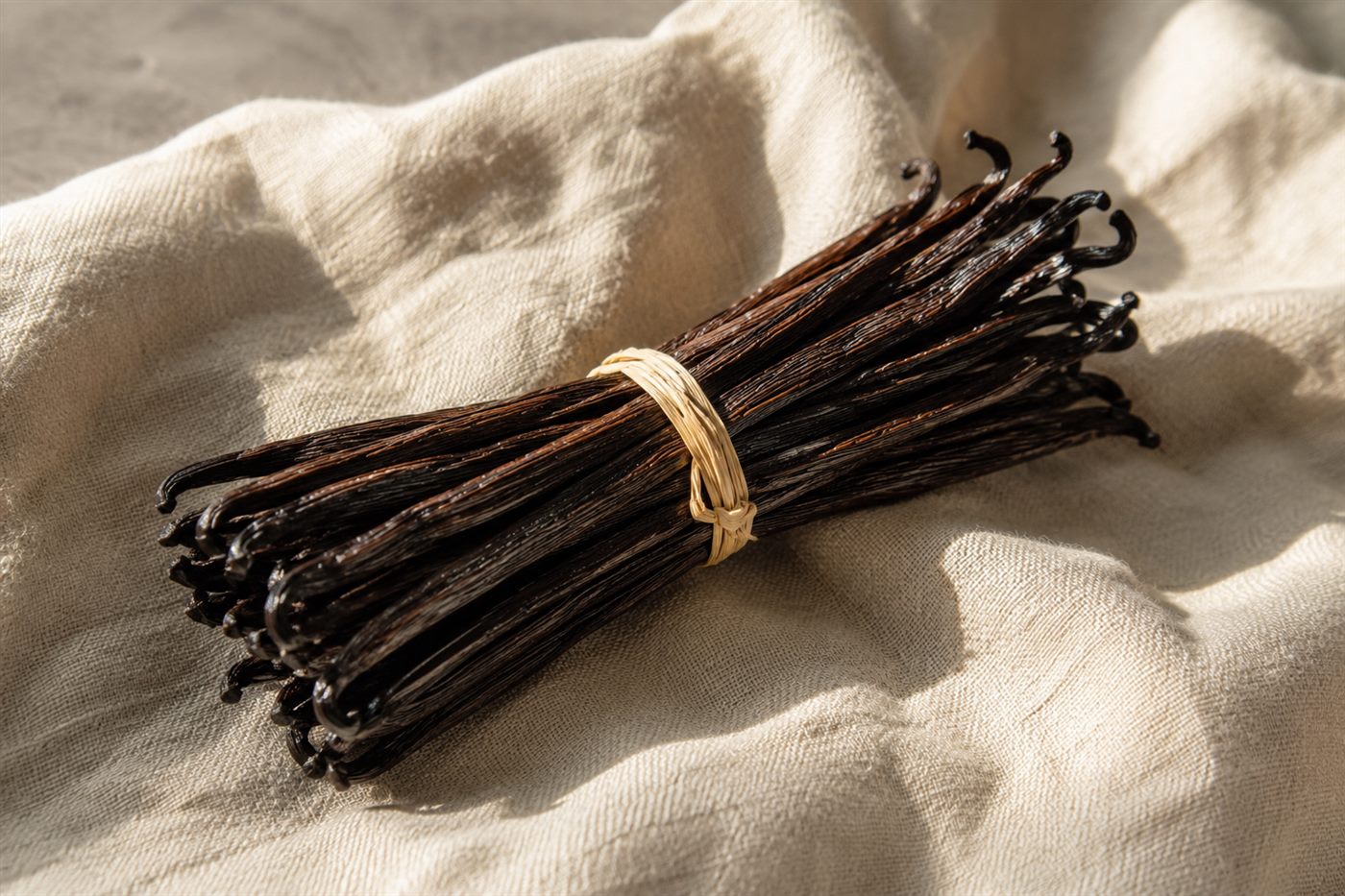 Botte de gousses de vanille Bourbon Gourmet liée au raphia, posée sur un lin crème en lumière naturelle