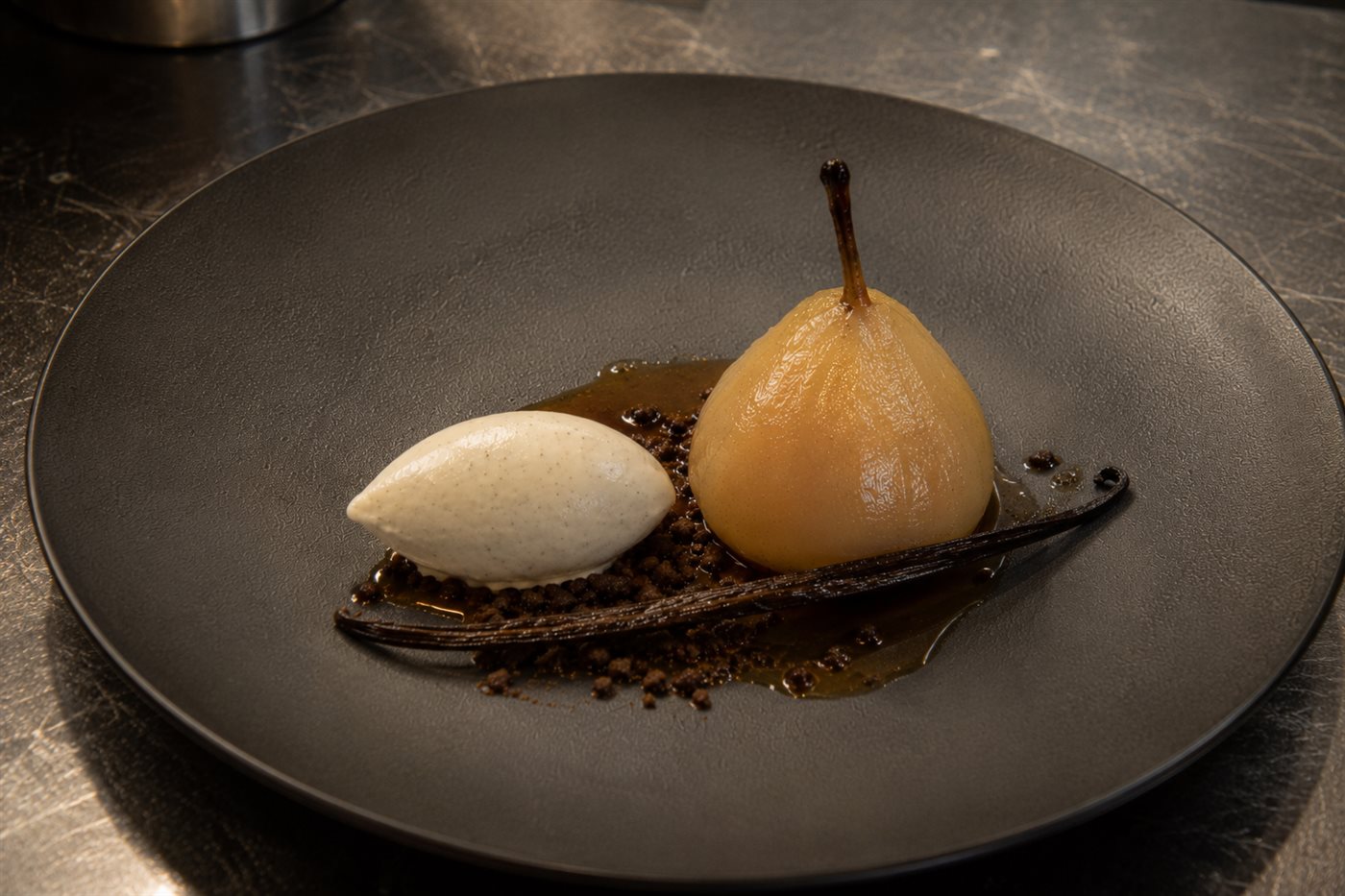 Dessert d'assiette gastronomique : poire pochée brillante de sirop, quenelle glacée et gousse de Pompona entière sur assiette sombre