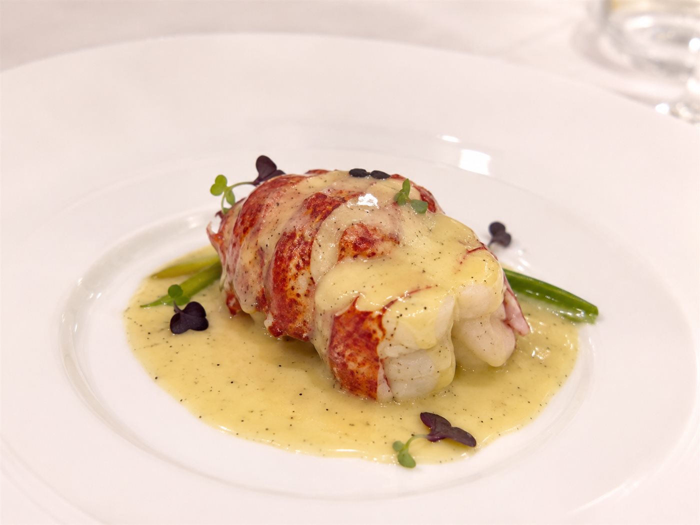 Queue de homard nappée d'un beurre blanc piqueté de grains de vanille, dressage gastronomique sur assiette blanche